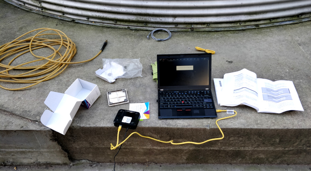 Laptop, modem, cables, and various manuals spread out on concrete.
